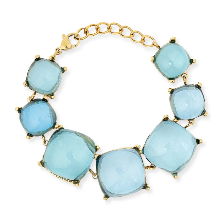 A gold-tone statement bracelet featuring seven large, light blue cushion-cut gemstones in prong settings, connected by a gold-tone chain extender and secured with a lobster clasp, shown on a plain white background.