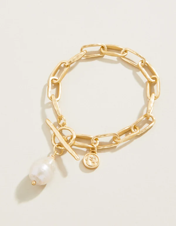 Gold chain bracelet with a pearl charm on a light beige background