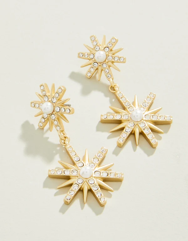 Gold star-shaped earrings with pearl centers on a light beige background