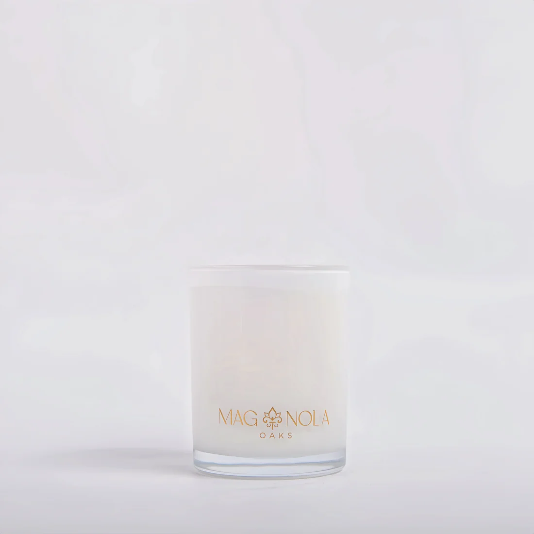 A frosted 8.5 oz glass jar candle with a gold foil logo reading 'MAG NOLA OAKS' on the front, set against a clean white background.background.
