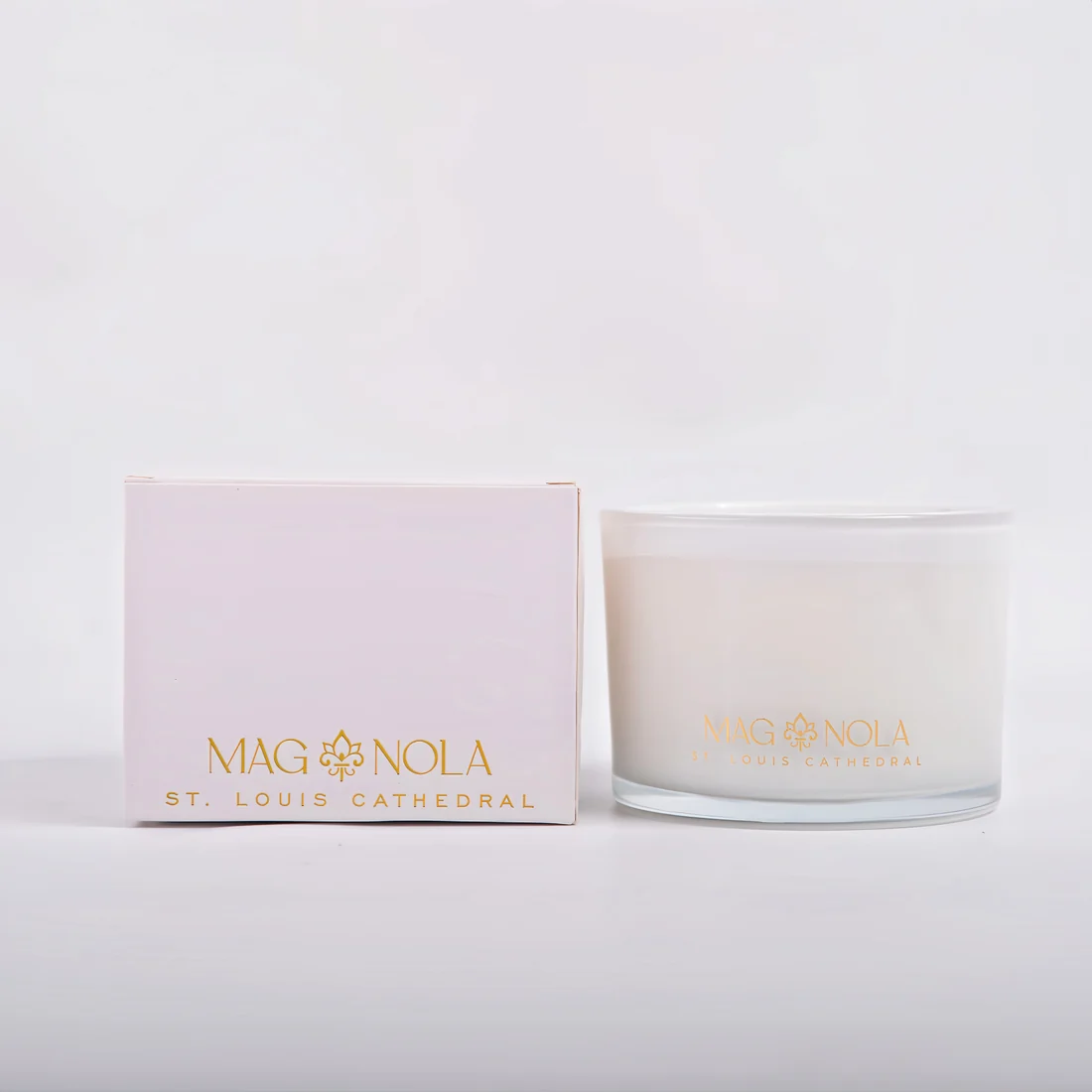 A frosted 8.5 oz glass jar candle with a white wax fill and gold foil branding that reads 'MAG NOLA' and 'ST. LOUIS CATHEDRAL' on a clean white background next to its container.