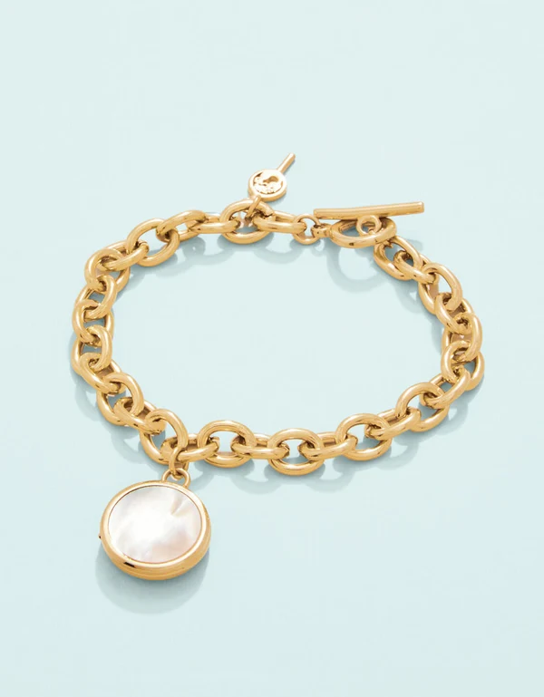 Gold bracelet with pearl locket on a light blue background. 