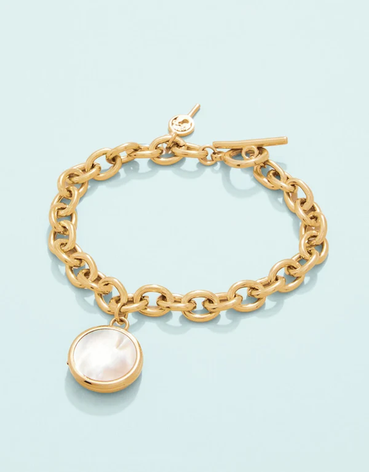 Gold bracelet with pearl locket on a light blue background. 