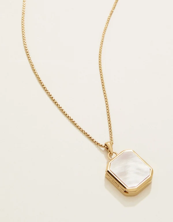 Gold necklace with a hexagonal pendant on a light beige background