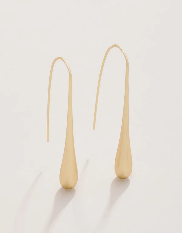 A pair of minimalist teardrop dangle earrings in a polished yellow gold finish, suspended from curved French hook ear wires, set against a clean off-white background.