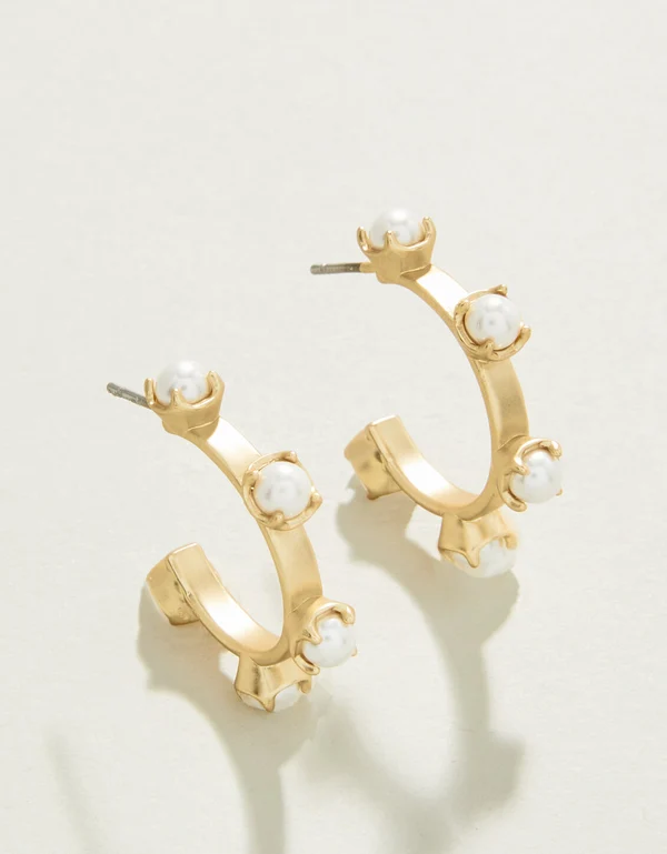 Gold hoop earrings with pearl-like stones on a light background