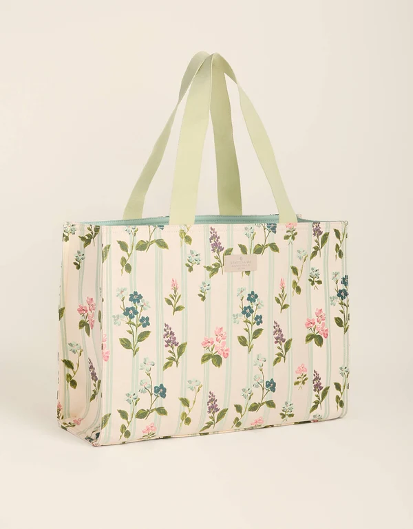 A tote bag featuring a floral pattern on a cream background, with light fabric shoulder straps, shown against a solid light beige background.