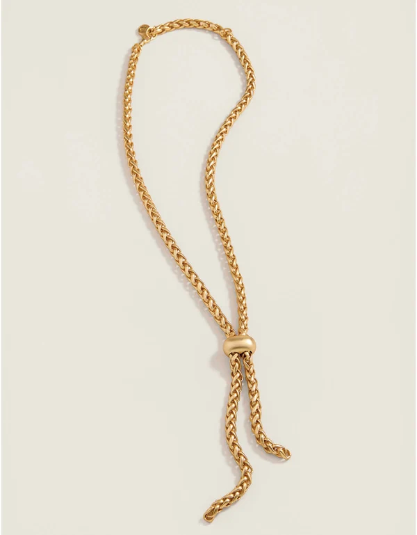 A gold-toned chain necklace with a knotted tassel detail, displayed on a light beige background.