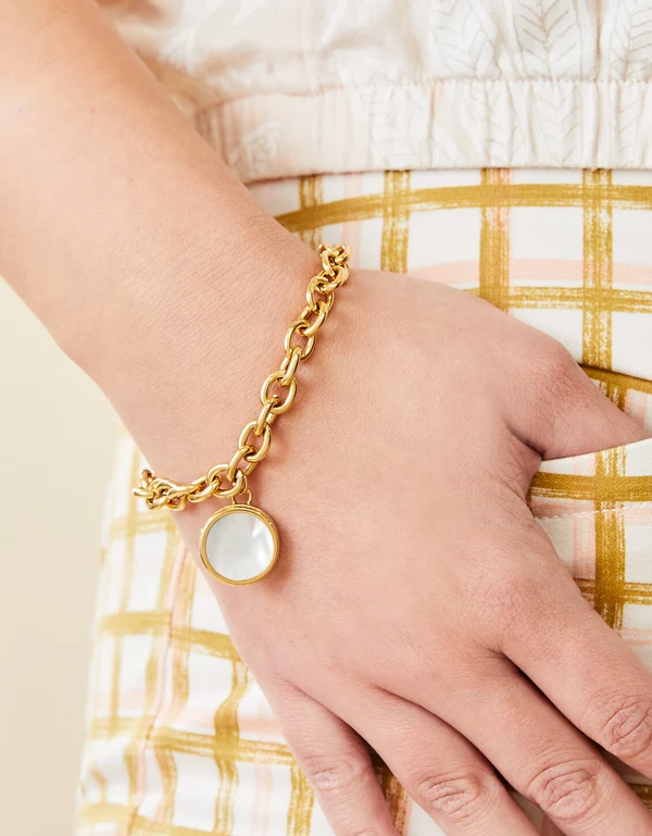 Close up of a gold bracelet with a pearl locket. 