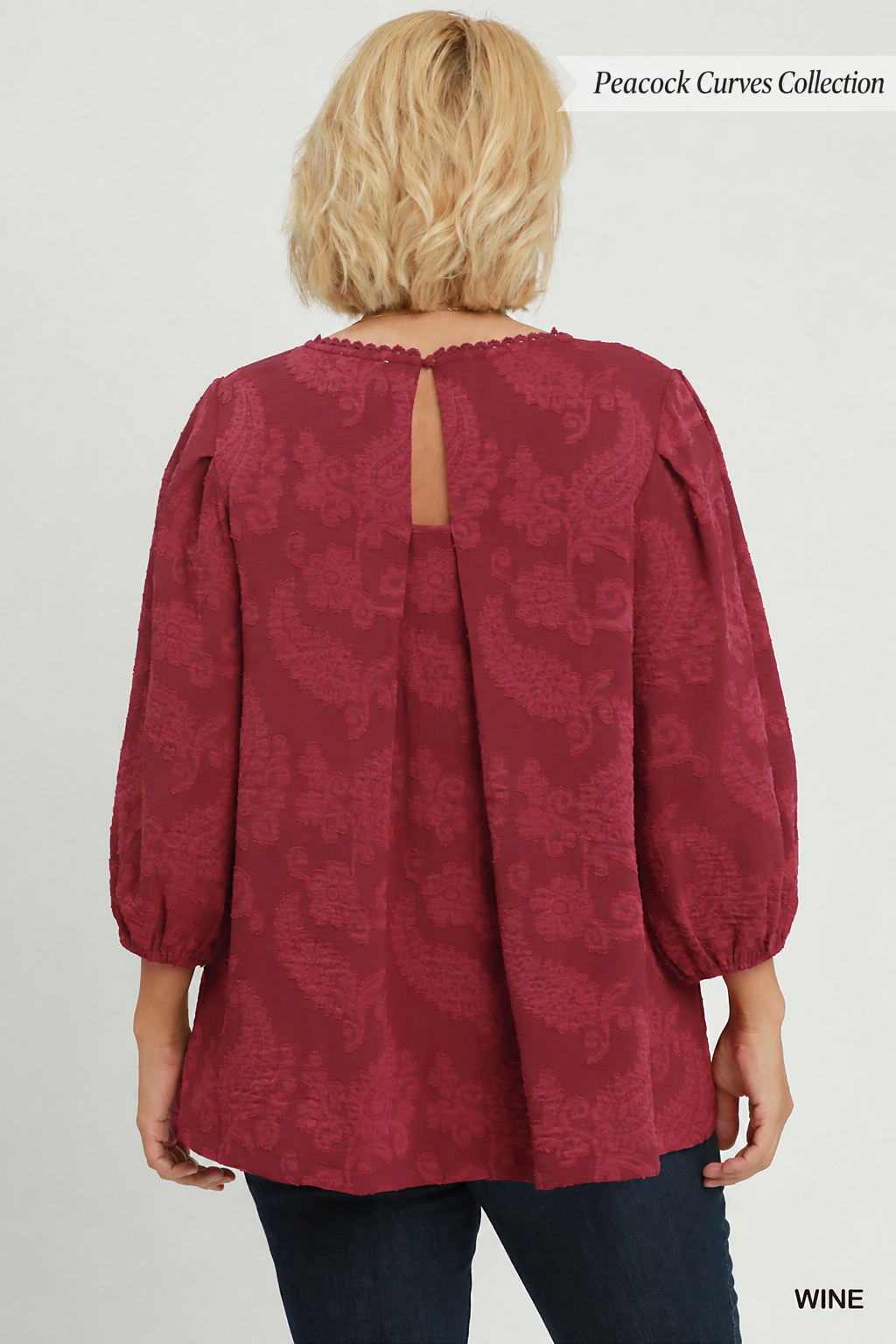A woman viewed from the back wearing a wine-colored long-sleeve blouse with a subtle paisley jacquard pattern and a keyhole back cutout.